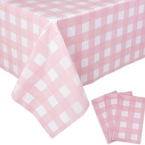May include: A pink and white checkered tablecloth and matching napkins. The tablecloth is draped over a table, with the corner of the cloth folded over. The napkins are neatly stacked, showcasing the same gingham pattern.