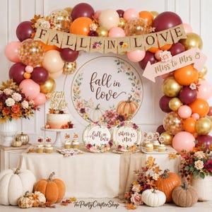 May include: A fall-themed party display featuring a balloon arch in burgundy, orange, and gold, a banner reading FALL IN LOVE, a sign saying Miss to Mrs, a cake, cupcakes, and plates with floral and pumpkin designs, and various decorative pumpkins.