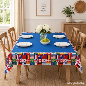 May include: A rectangular tablecloth with a solid blue center and a border featuring a repeating pattern of various international flags. The tablecloth is draped over a wooden dining table set with four chairs, white plates, and napkins.