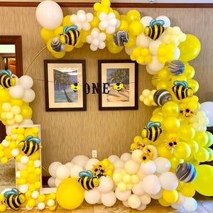 Puede incluir: Decoraci&oacute;n festiva para fiestas con una gran disposici&oacute;n de globos amarillos y blancos, con detalles de abejas y flores. La exhibici&oacute;n incluye un gran n&uacute;mero "1" y un arco circular, con la palabra "ONE" en una pancarta.