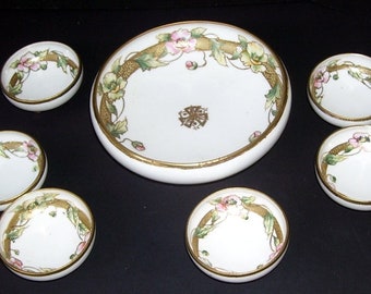 May include: A set of seven white porcelain bowls with gold trim and floral designs. The bowls are arranged in a circle with a larger bowl in the center.