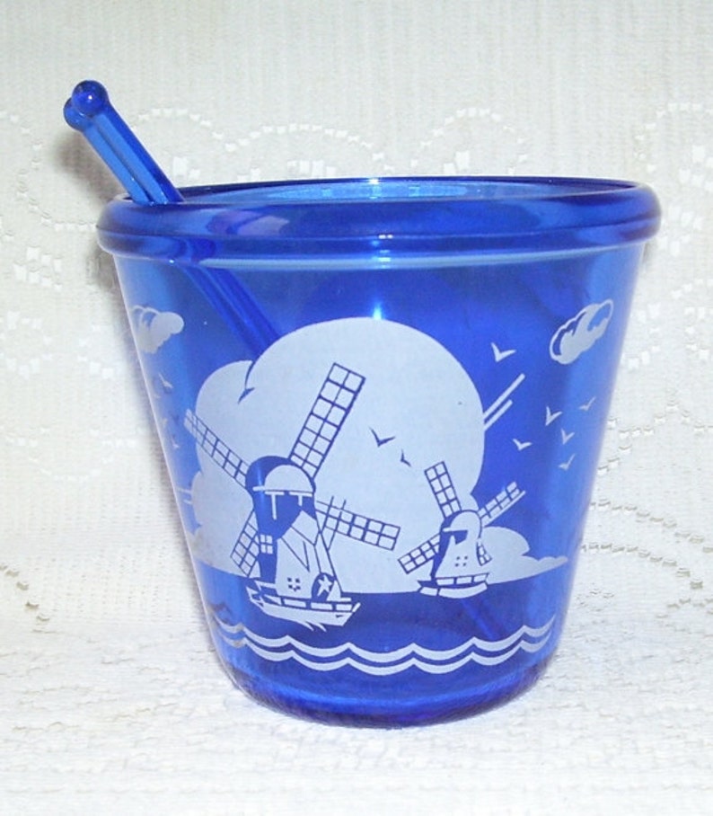May include: Cobalt blue glass sugar bowl with a white windmill design and a matching stirrer. The bowl has a rounded bottom and a wide rim.