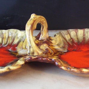 May include: A ceramic serving dish with three sections and a handle. The dish is decorated with a yellow, brown, and red glaze.
