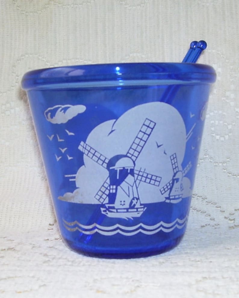 May include: Cobalt blue glass sugar bowl with a white windmill and seagull design. The bowl has a matching cobalt blue glass stirrer.