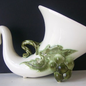 May include: White ceramic vase shaped like a cornucopia with green grape leaves and grapes.