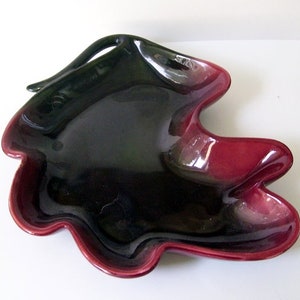 May include: A black and burgundy ceramic serving dish with a unique, organic shape. The dish has a glossy finish and a raised handle.