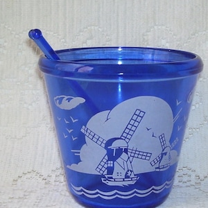 May include: A cobalt blue glass cup with a white windmill design and a matching blue plastic stirrer. The cup has a white rim and a white base.