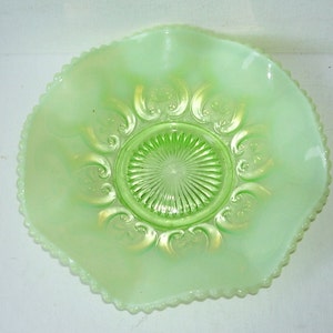 May include: A green glass bowl with a scalloped edge and a decorative design in the center. The bowl is made of Depression glass.