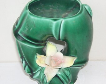 May include: A green ceramic vase shaped like a bamboo stalk with a white and pink flower.