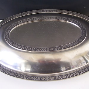 May include: A silver oval serving dish with two handles. The dish has a decorative border around the edge.