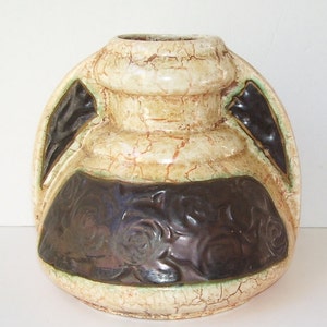 May include: A ceramic vase with a cream-colored, crackled finish. The vase has a dark brown, textured band with a floral design and dark accents. The vase has a rounded shape with two side handles.
