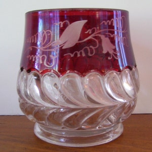 May include: A ruby red glass goblet with a clear, cut glass base. The top of the goblet has a white etched floral design.