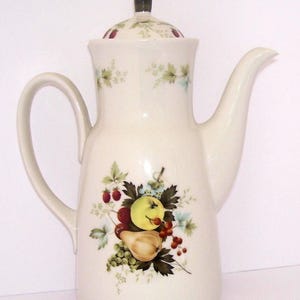 May include: White ceramic coffee pot with a black knob on the lid. The pot has a floral design with fruit and green leaves.