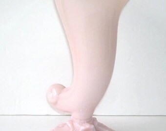 May include: A pale pink, vintage-style vase with a flared top and a curved, horn-like body. The base features a decorative, petal-like design. This elegant vase is perfect for displaying flowers or as a decorative accent piece.