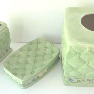 May include: A set of four green ceramic bathroom accessories with a quilted design. The set includes a toothbrush holder, soap dish, and tissue box cover.