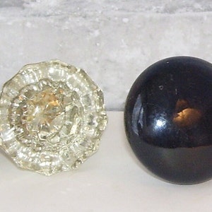 May include: Four different door knobs. One is white ceramic, one is clear glass with a floral design, one is black and one is a dark brown.