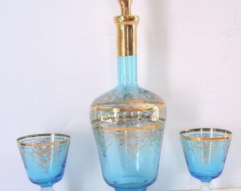 May include: A set of three blue glass decanters with gold accents. The decanters have a decorative design and are perfect for serving liquor.