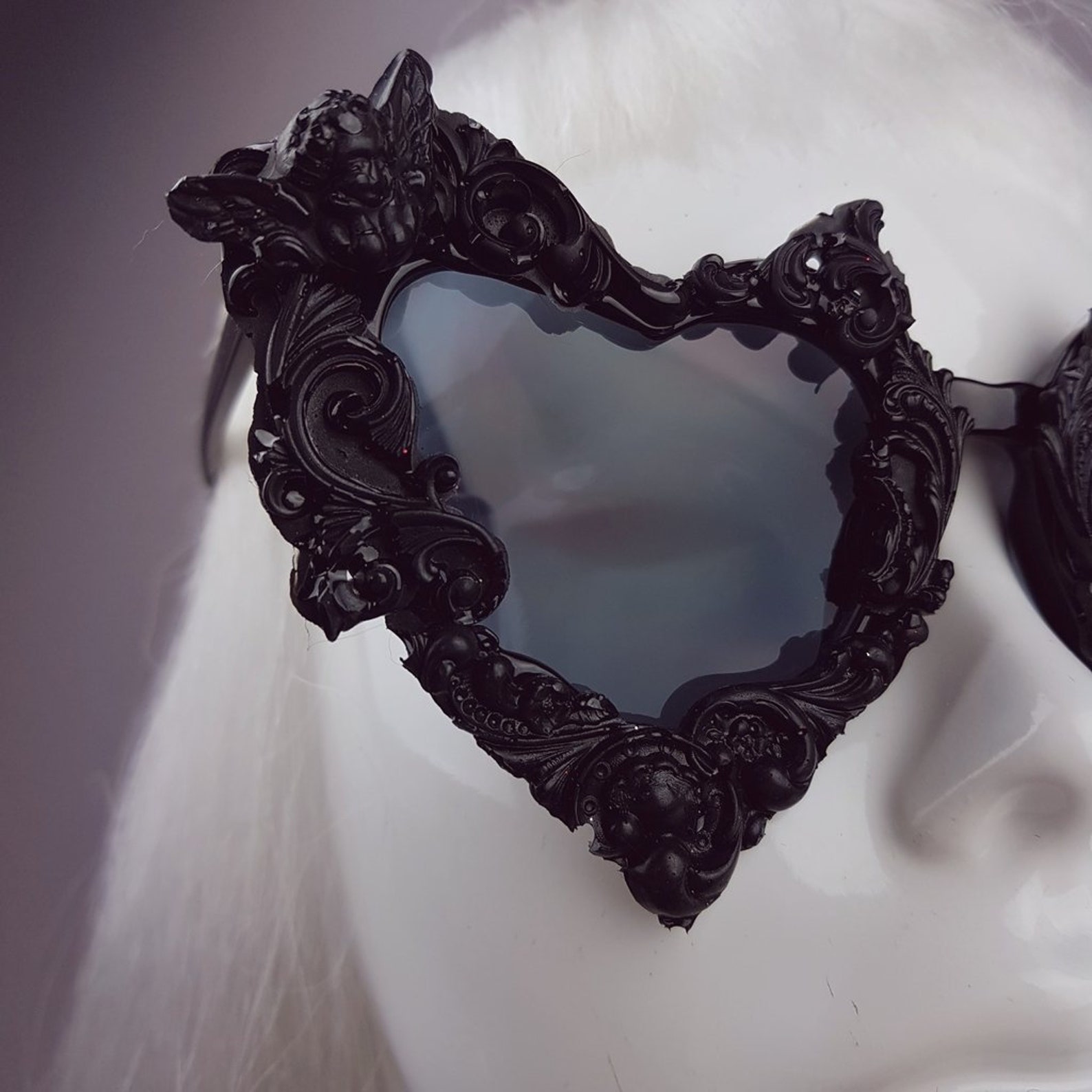 Close-up of black gothic heart sunglasses with ornate baroque detailing and bat-wing accents on a mannequin face
