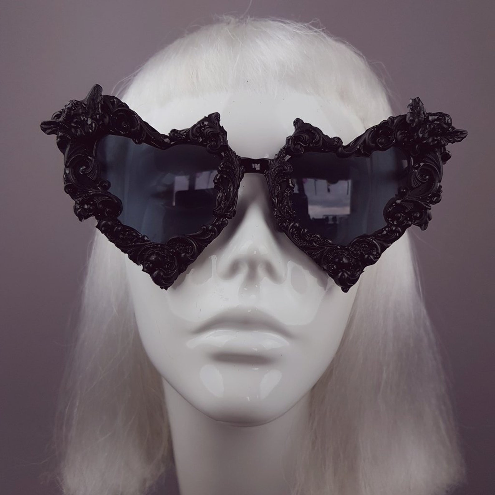 Front view of black baroque heart sunglasses with gothic bat details, worn on a mannequin with platinum blonde wig