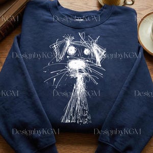 May include: Navy blue sweatshirt featuring a whimsical white line drawing of a dog's face. The dog's features are created with scribbled lines, giving it a playful, artistic look. The text "DesignbyKGM" is printed around the sweatshirt.