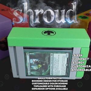 May include: A lime green and gray plastic card storage case featuring a top-loading slot holding a single trading card. The case has a tree symbol on the top lid. Several other colorful storage cases are visible in the background.