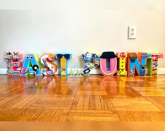 May include: Colorful foam letters spelling "EAST POINT" decorated with 1980s and 1990s pop culture icons, including a boombox, a cassette tape, a video game, a basketball, a Pac-Man, and a crown.
