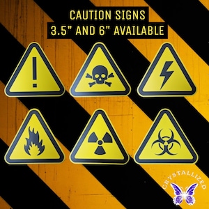 May include: A collection of yellow triangular caution signs with black borders and symbols, including an exclamation point, skull and crossbones, lightning bolt, flames, radiation symbol, and biohazard symbol. Text at the top reads "CAUTION SIGNS 3.5" AND 6" AVAILABLE."