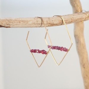 Puede incluir: Aretes de aro de oro con forma de diamante geométrico y una fila de piedras preciosas rosadas.