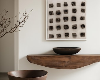 May include: A minimalist interior design with a wooden shelf and two brown bowls. A framed black and white abstract art piece hangs on the wall behind the shelf.
