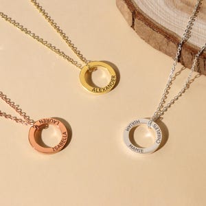 Könnte beinhalten: Drei goldene Halsketten mit runden Anhängern. Jeder Anhänger trägt einen anderen Namen: "ISABELLA LAUREN", "MAMIE CHARLES MIRIAM" und "ALEXANDER".