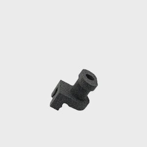 Può includere: Un oggetto geometrico grigio scuro con un'estensione cilindrica e una base quadrata. L'oggetto ha una superficie ruvida e strutturata, forse realizzata con un materiale poroso. Il design suggerisce un componente meccanico o industriale.