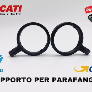 Könnte beinhalten: Zwei schwarze, kreisförmige Motorradkotflügelhalterungen mit griffartiger Verlängerung. Das Ducati Monster-Logo und das Ducati Corse-Emblem sind sichtbar. Der Text "SUPPORTO PER PARAFANGHI" ist ebenfalls vorhanden.