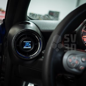 Puede incluir: Primer plano del interior de un coche con un indicador digital que muestra "20%" y un volante con botones. El indicador es azul y el volante es negro.