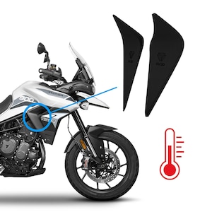 Op de afbeelding: Een wit en zilver Triumph Tiger 900 motorfiets met zwarte accenten, en twee zwarte beschermpanelen. Een rode thermometer afbeelding is ook aanwezig.
