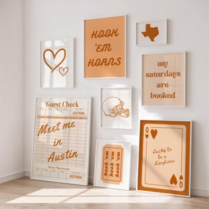 May include: A collection of framed art prints with a warm, neutral color palette. The prints feature various designs, including a heart, a football helmet, a Texas outline, and phrases like "Hook 'em Horns" and "Meet me in Austin."