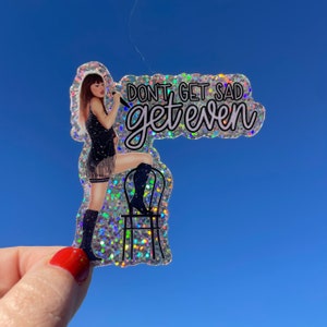 May include: A sparkly silver sticker with a woman in a black sequined dress and boots sitting on a black chair. The sticker says "Don't get sad get even".