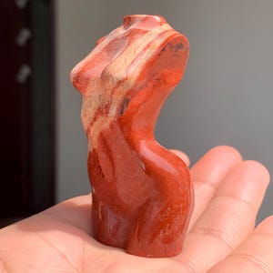 May include: A red and white striped stone sculpture of a human torso.