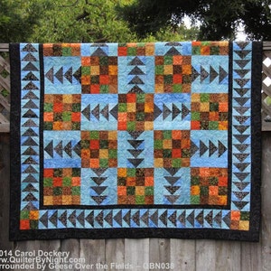 May include: A quilt with a patchwork design featuring a variety of colors and patterns. The quilt is bordered with a black and blue trim. The quilt is titled "Surrounded by Geese Over the Fields - QBN038".
