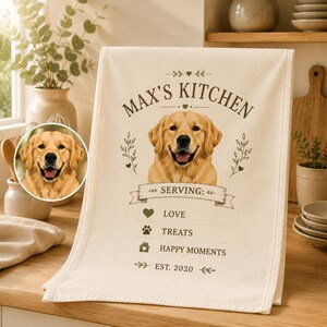 Pode incluir: Um pano de prato cor de creme com o retrato de um golden retriever e o texto "MAX'S KITCHEN" no topo. Abaixo do cão, o texto diz "SERVING: LOVE", "TREATS" e "HAPPY MOMENTS" com ícones, seguido de "EST. 2020" na parte inferior.