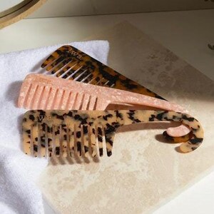 May include: Three tortoiseshell combs, one with a pink handle, one with a brown handle, and one with a black and white handle.