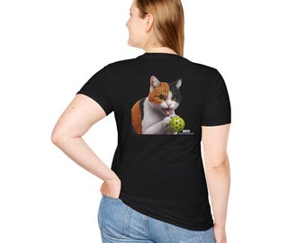 以下が含まれることがあります： 緑色のボールで遊ぶ三毛猫のグラフィックがプリントされた黒いTシャツ。猫の下に「OTIS」という文字がプリントされています。