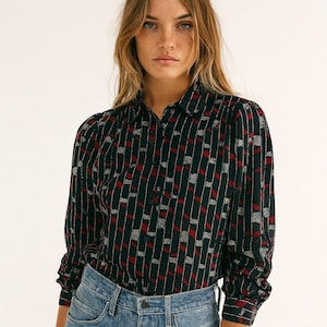 May include: A long-sleeved button-down shirt with a geometric pattern. The shirt features a dark background with vertical stripes of red and white geometric shapes. The shirt has a collared neckline and buttoned cuffs. The model is wearing blue jeans.