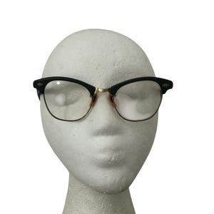 May include: Black and gold-rimmed eyeglasses with clear lenses. The frames have a classic, retro design, with a black upper frame and gold-colored lower rims and bridge. The glasses are displayed on a white mannequin head.