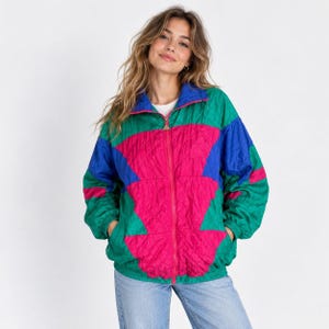 May include: A long-sleeve zip-up jacket featuring a vibrant color-blocked pattern in shades of bright green, hot pink, and royal blue. The jacket has a high collar, a full-length front zipper, and elasticized cuffs and hem for a gathered fit.