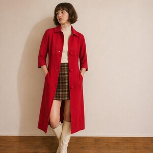 May include: A long, bright red coat with three-quarter sleeves and large buttons. The coat is worn over a cream-colored turtleneck and a plaid skirt. The outfit is completed with knee-high cream-colored boots. The coat has pockets.