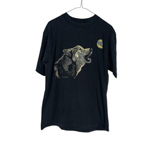 May include: A black short-sleeve t-shirt featuring a graphic print of a wolf howling toward a yellow moon. The wolf is depicted in shades of brown, gray, and white, with its mouth open. The design is centered on the chest of the garment.