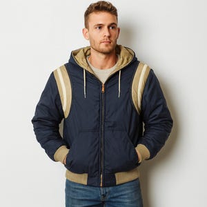 Könnte beinhalten: Marineblaue Kapuzenjacke mit beigen Akzenten an Schultern und Kapuze. Die Jacke hat einen Frontreißverschluss, eine Fronttasche sowie gerippte Bündchen und Saum. Die Jacke hat ein beiges Innenfutter.