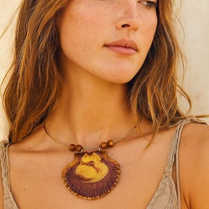 May include: A seashell pendant necklace with a gold-colored wire and wooden beads. The pendant is a mix of brown and yellow, resembling a scallop shell. The necklace is worn around the neck.
