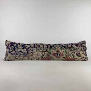 May include: A long, rectangular lumbar pillow featuring a woven textile cover with a distressed, vintage-style pattern in shades of deep navy blue, muted pink, cream, and sage green, displaying intricate floral and geometric motifs throughout.