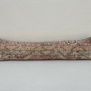 May include: A long, rectangular cushion with a colourful, floral pattern. The cushion is made of a soft, woven fabric and has a beige, pink, and brown colour scheme.